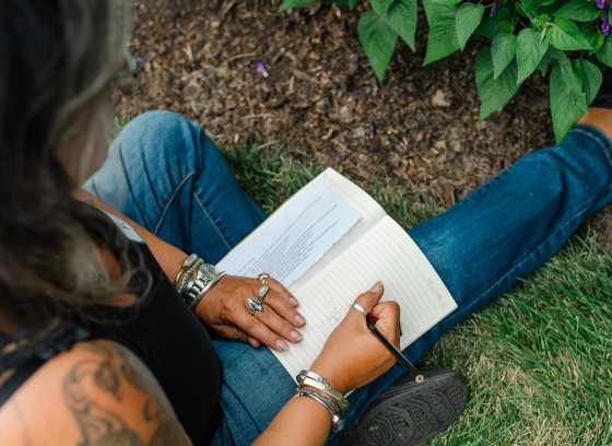 Closeup of person writing in a notebook while sitting in a garden.