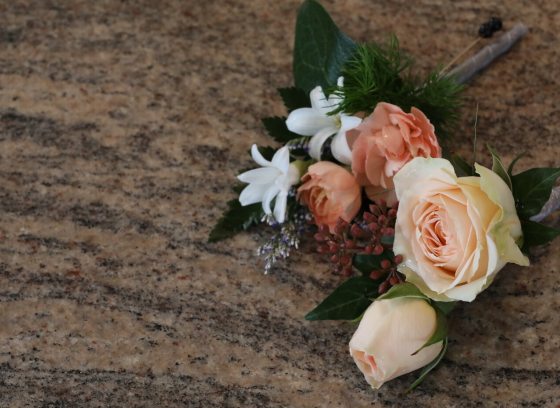 Two small floral lapel pieces laying on a wood graid table.