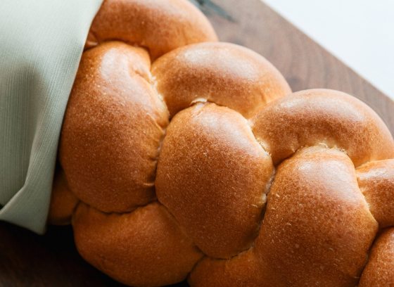 A close-up, high-angle view of a golden brown, freshly baked loaf of braided bread.