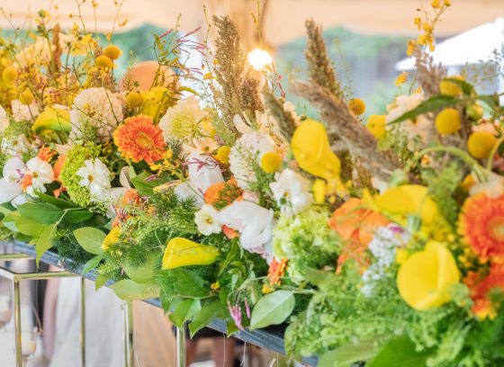 A tablescape of yellow, orange, and white flowers in tall mirrored vases.