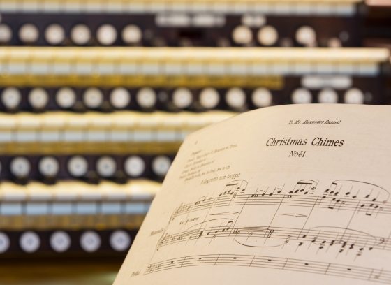Closeup of an organ keyboard with sheet music for Christmas Chimes Noel in the right foreground.