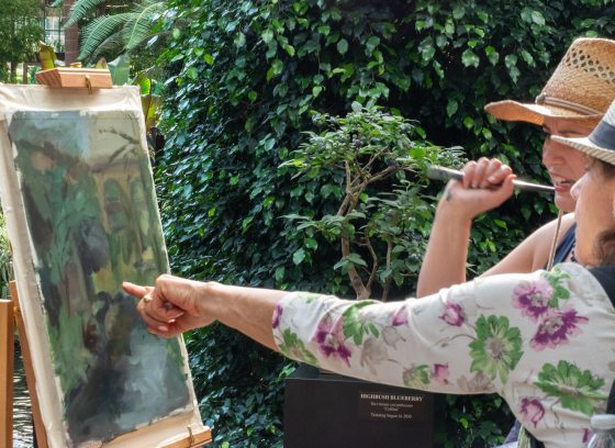 A close-up of two art students or artists pointing at and reviewing a landscape painting in progress during an painting class.