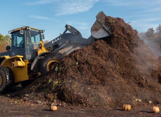 A yellow tractor on a steaming pile of dark brown composted soil.
