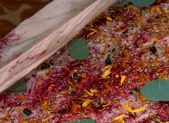 The fabric is covered with a dense layer of dried organic matter, including deep pink or purple petals, bright orange-yellow flower fragments, and small green eucalyptus leaves.