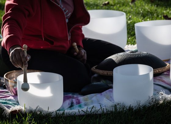 A person sitting outdoors on a blanket, surrounded by various instruments used for a sound bath or meditative practice.