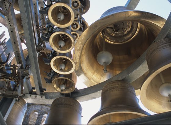 View from below of large and small carillon bells, awaiting installation into stone tower visible at bottom left.