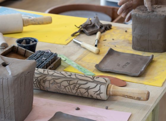 A work table with clay, rolling pins, and tools to make clay pots.