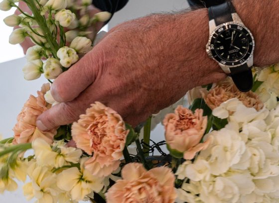 Hands, with a black wrist watch, working with a floral arrangement.
