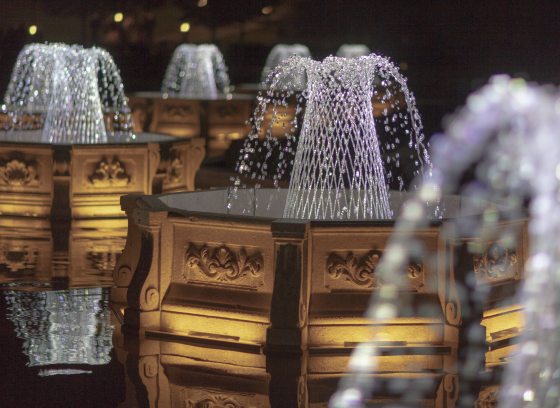 Basketweave fountains in octagonal basins lit by sparkling white light against a black sky.