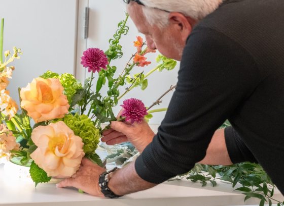 A person in a black shirt, creating a floral design featuring peach and magenta flowers.