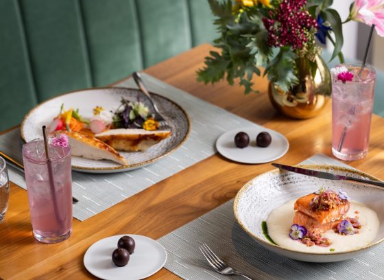 A table in a fine dining restaurant featuring several plates of food and a vase of flowers. 