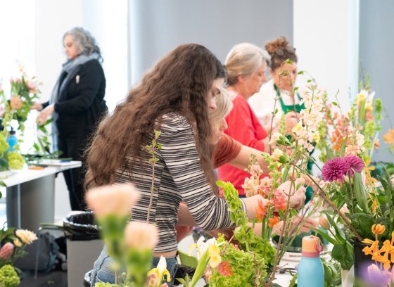 A classroom image of people working at tables crafting floral arrangements.