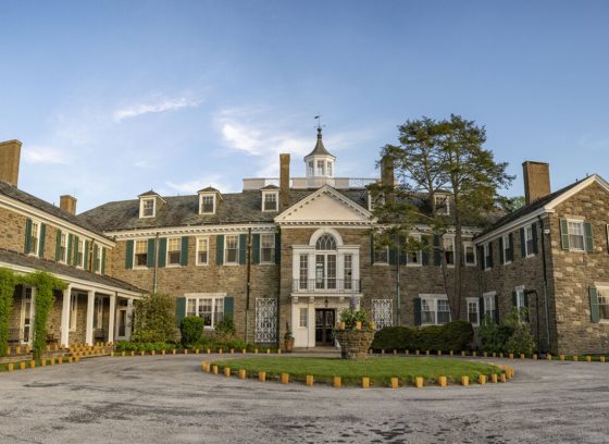 A very large stone estate with brown stone, cream trim, set against a bright blue sky. 