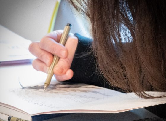 A person with their head bent down, drawing in a sketchbook. 