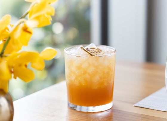 A autumn inspired cocktail in a highball glass, on a light wood table. 