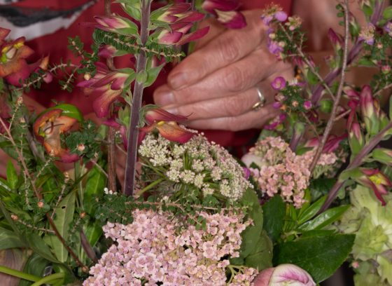 An upclose image of a person's hand arranging stems in a floral arrangement.