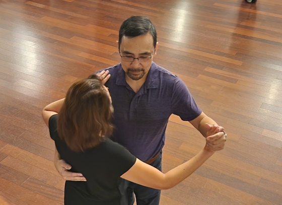 Two people ballroom dancing on a wooden floor.
