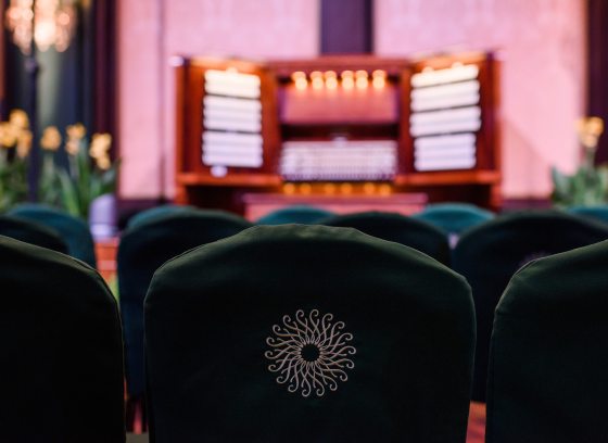 Images of empty green chairs with the Longwood logo on back, awaiting a performance, with a blurred image of an organ console in the background.