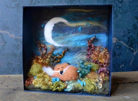 A needle felt shadowbox scene featuring a red fox, a crescent moon, and a green foreground.
