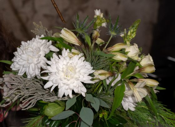 An all white floral arrangement set against a moody dark background.
