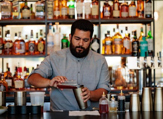 A bartender, mixing a cocktail behind a wood bar. 
