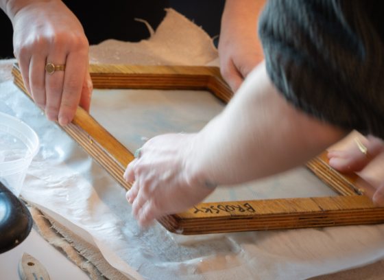 Two people holding a wood frame and making paper.