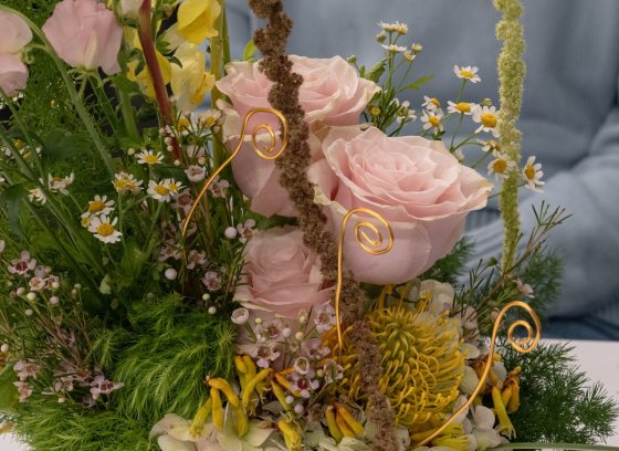 A close up of a floral arrangement featuring light pink roses, yellow foliage, and gold accents. 
