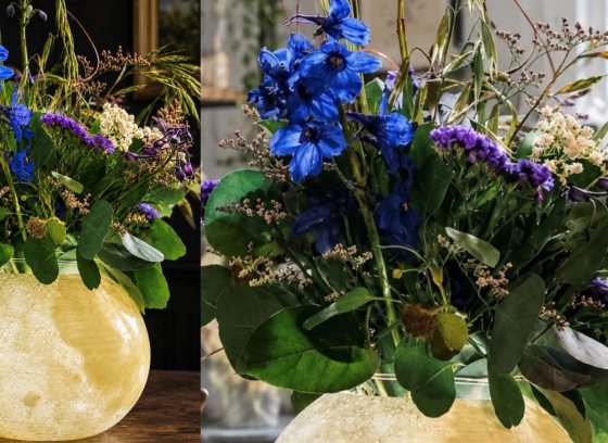 A floral arrangement with an illuminate moon vase and blue and purple flowers.