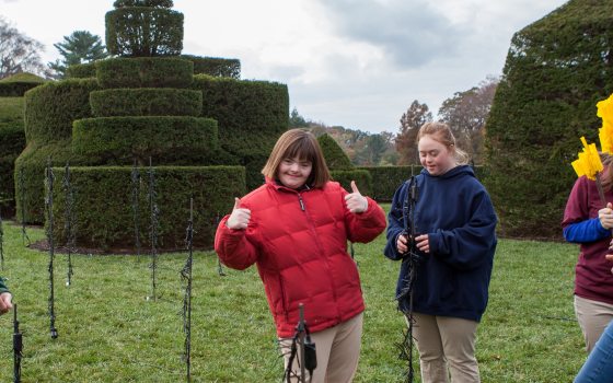 two students smile at the camera with one putting thumbs up in front of the topiary garden