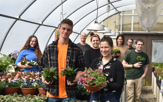a group of students holding plants in a greenhouse 
