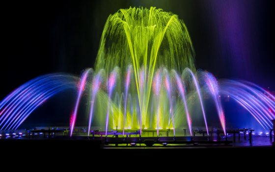 illuminated lime green fountain rises above blue and pink arches of water