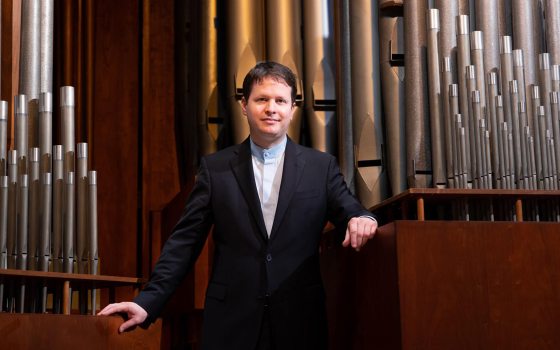 Adult standing in front of organ pipes.