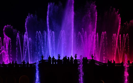 silhouettes of people watching fuchsia, purple, and red fountains rise high against a black sky