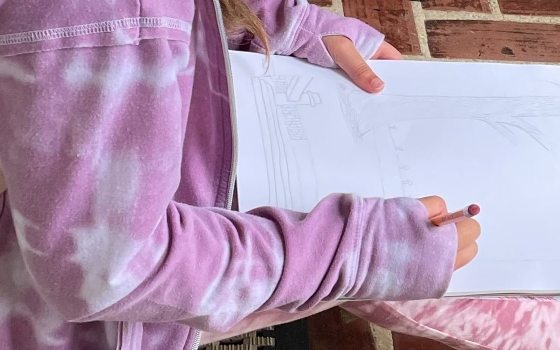 a person with pink top and pants draws with a pencil in a spiral sketchbook