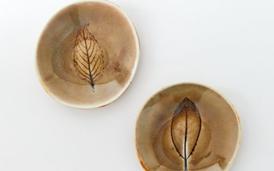 two small pottery bowls with leaf patterns in the center