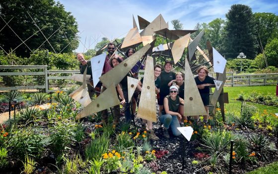 A group of people standing inside an outdoor geometric sculpture in a garden bed.