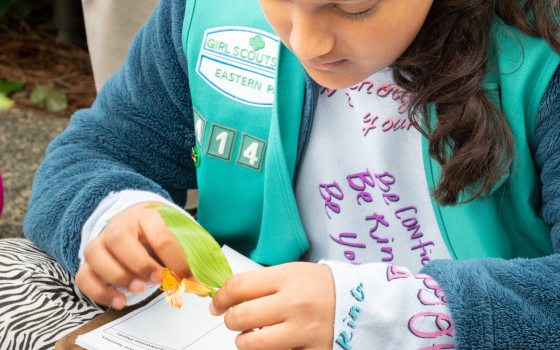 A girl scout sitting at a table writing in a notebook.