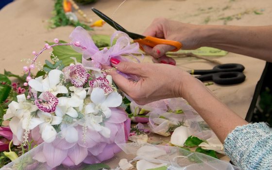 A person's hands holding scissors while creating a floral arrangement.