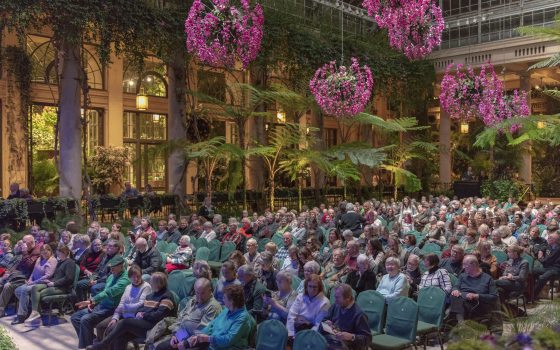People seated inside the Longwood Gardens Conservatory awaiting a concert to begin.