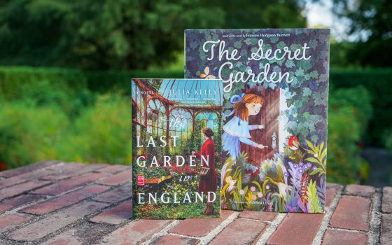 Two books on a brick wall—entitled "The Secret Garden" and "The Last Garden in England," against an outdoor background of green gardens and trees.