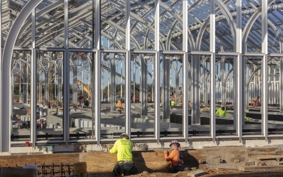 Construction workers amid an open framework of arched metal columns and beams.