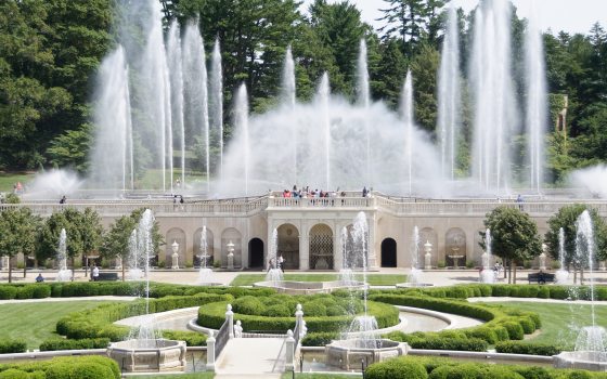 A large display of fountains shoots skyward above a stone facade, with green gardens and smaller fountains in the foreground.