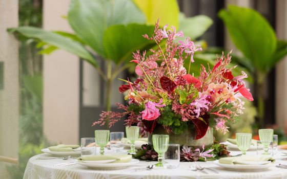 Closeup of table setting whose main focus is a floral arrangement in hues of pink, red, and green.