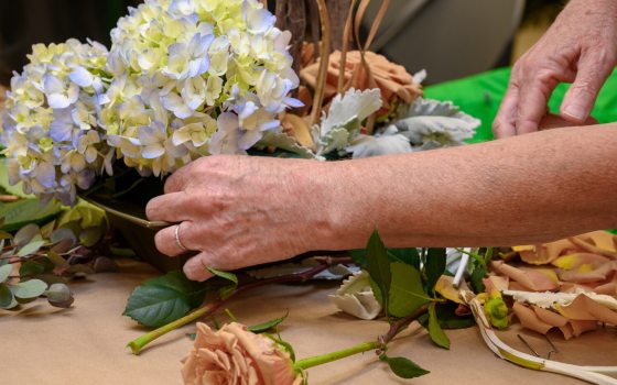 A person creating a floral arrangment out of white and purple hydrangeas.