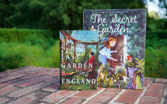 Two books: The Last Garden in England and The Secret Garden, stand atop a brick wall with a green garden in the background.