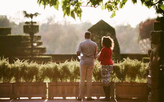 A man and woman gazing out over the topiary garden filled with evergreen trees, trimmed into circular and square-like shapes.