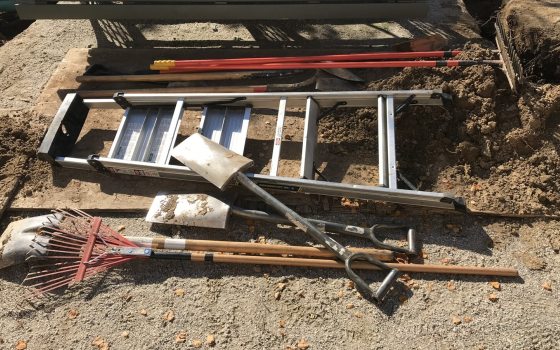 Shovels and a ladder laying on the dirt ground.