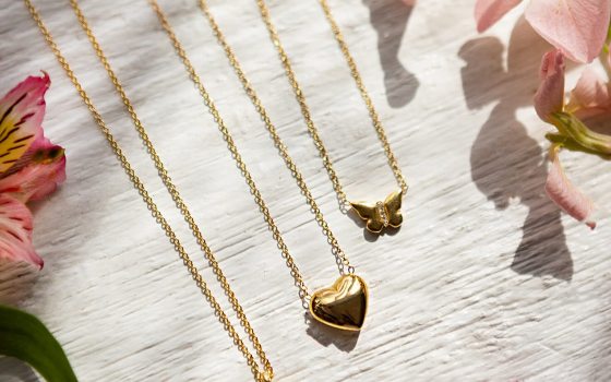 Three gold necklaces laying flat on a white table with flowers around them,