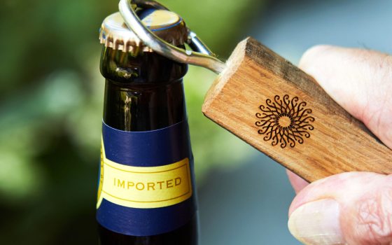 A person using a wooden bottle opener to open a bottle. 