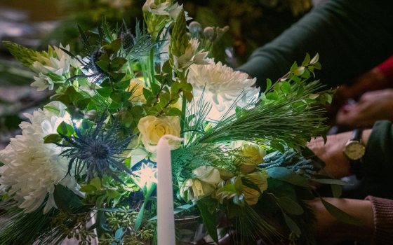 A holiday flower bouquet featuring white florals, white lights, and a candle in the center.